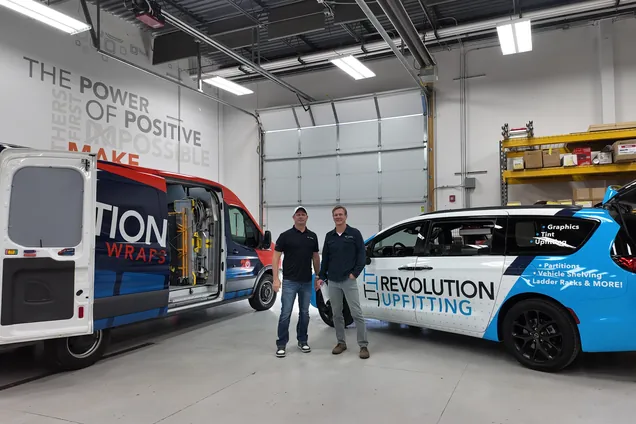Revolution Upfitting owners Ryan and Scott in the shop between a Revolution Wraps van and a Revolution Upfitting minivan