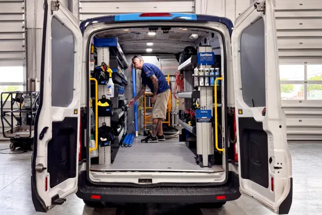 Technician organizing a Sortimo shelving upfit through the open rear doors of a work van in the Revolution Upfitting shop