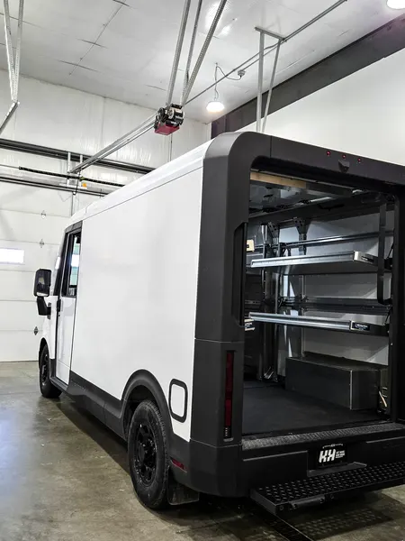 Walk-in box truck with its rear roll-up opening fitted with shelving, parked inside a shop