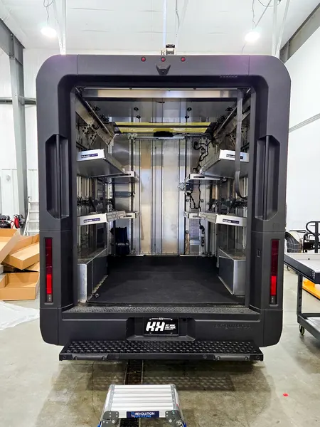 Rear view into an upfitted box truck body with shelving down both walls and a rubber floor
