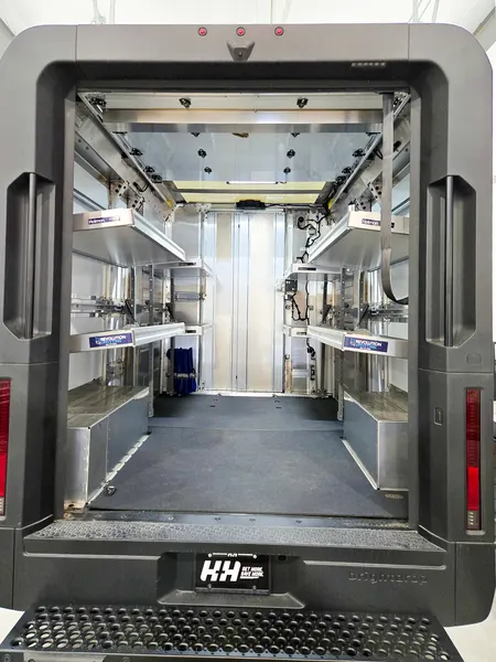 Box truck interior seen from the rear bumper, with shelving on both sides and ceiling lighting