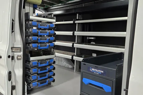 Stack of blue Sortimo parts cases beside wall shelving and a Revolution drawer unit in the Dworak Plumbing van