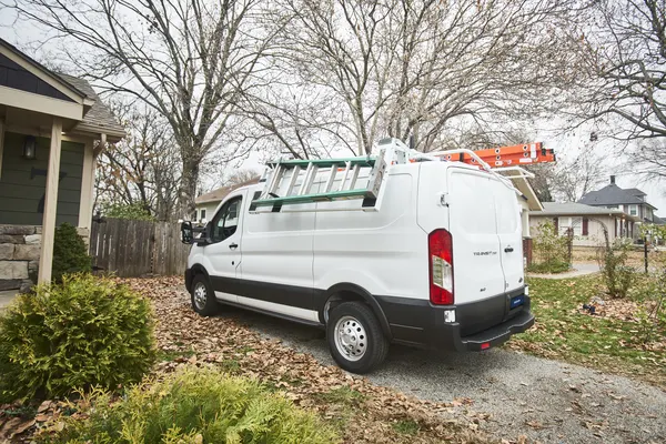 White Ford Transit cargo van with a roof ladder rack parked in a residential driveway