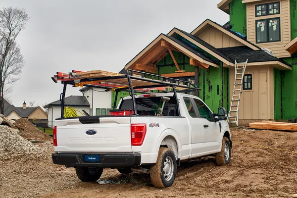 White Ford F-150 pickup with a full-length ladder rack loaded with lumber at a home construction site