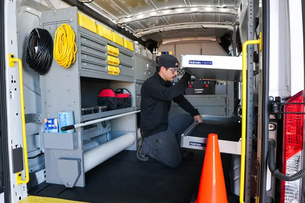 Technician kneeling beside a Holman drawer inside a van fitted with yellow-bin shelving