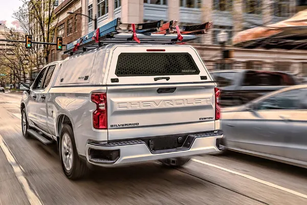 White pickup with a SmartCap and roof ladder rack driving through a city street