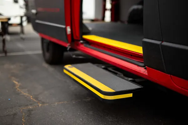 Automatic mechanical side step deployed under the sliding door of a red and black work van