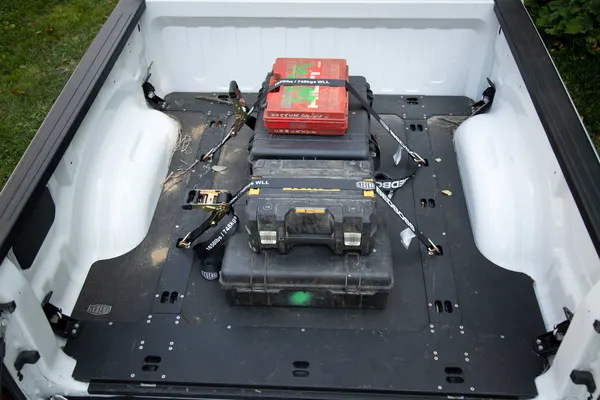 Bed Boss tie-down floor in a white pickup bed with tool cases strapped to the anchor points