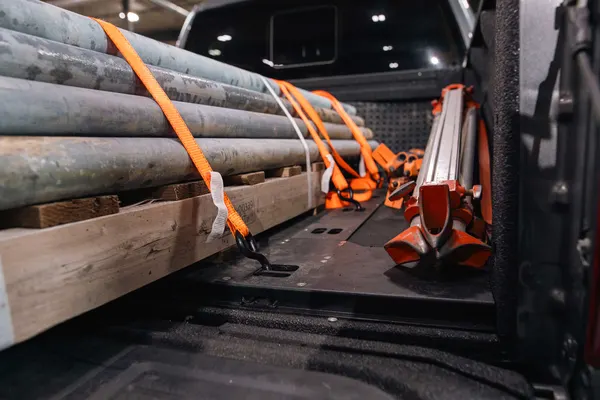 Pipe and a pipe stand strapped down to a Bed Boss floor system with orange ratchet straps