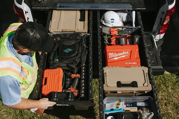 Technician in a safety vest reaching into slide-out truck bed drawers loaded with power tools