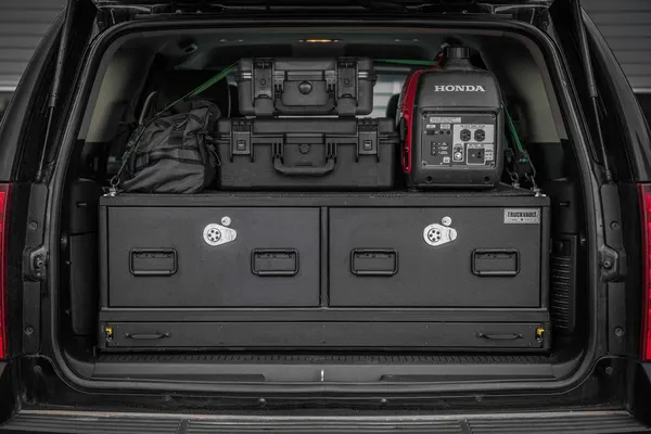 Two-drawer TruckVault in a full-size SUV with tie-down rails securing cases and a generator on the lid