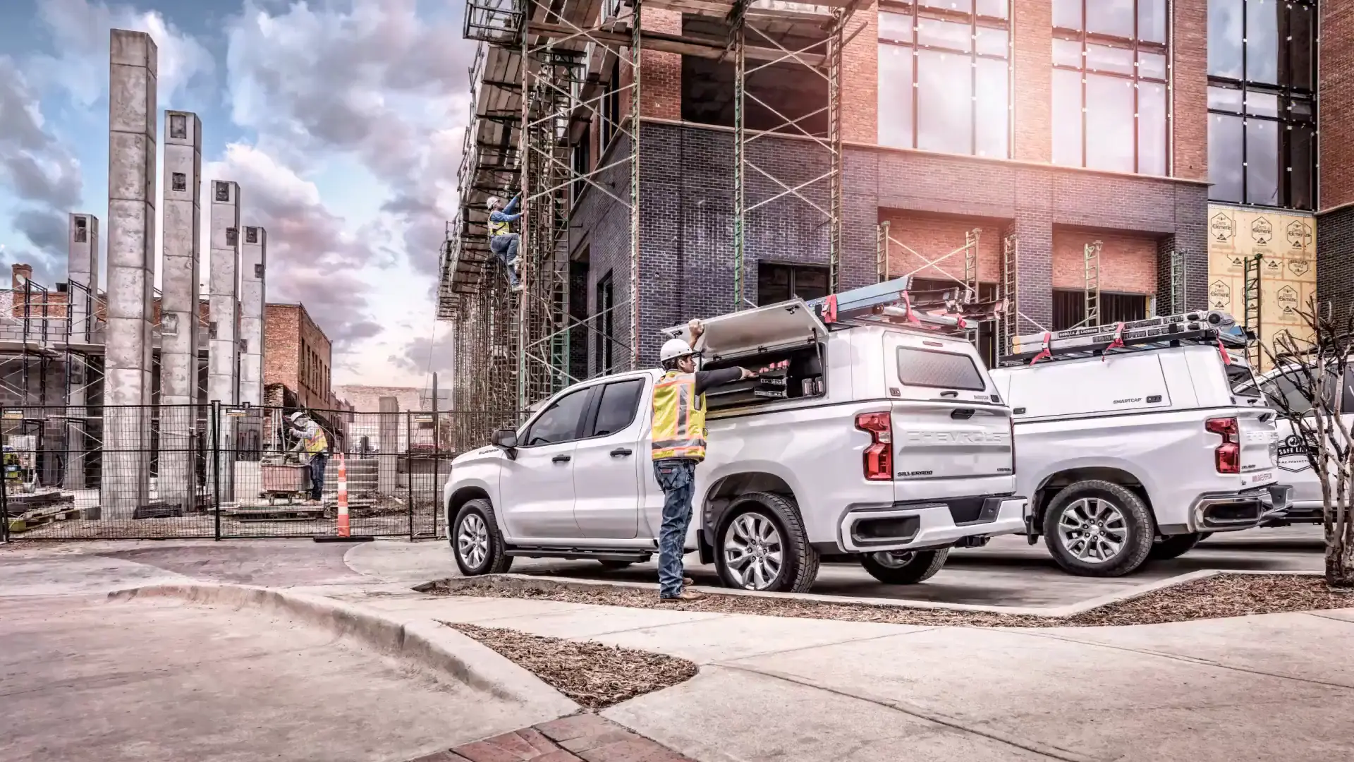 Worker at a white pickup fitted with a SmartCap truck cap and roof ladder rack at a construction site