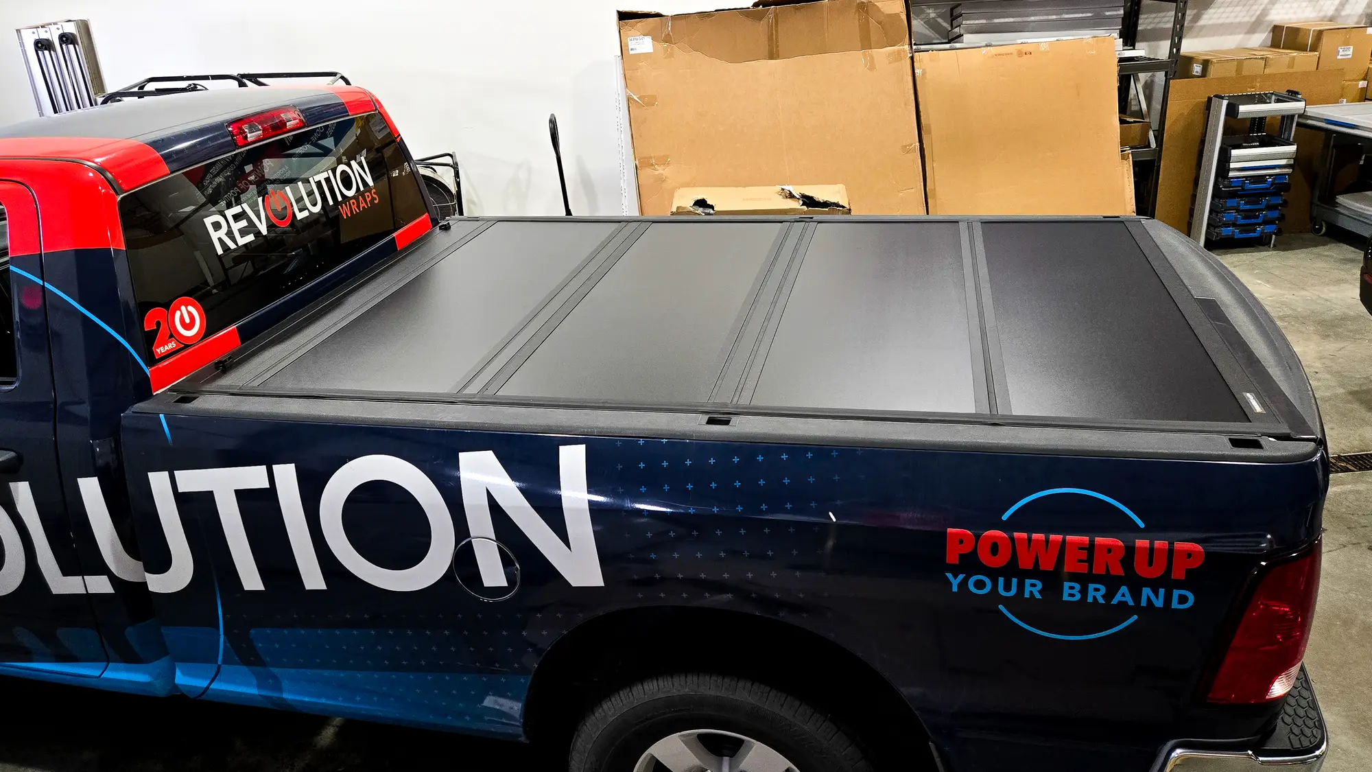 Revolution Wraps pickup with a hard folding tonneau cover over the bed, parked in the shop