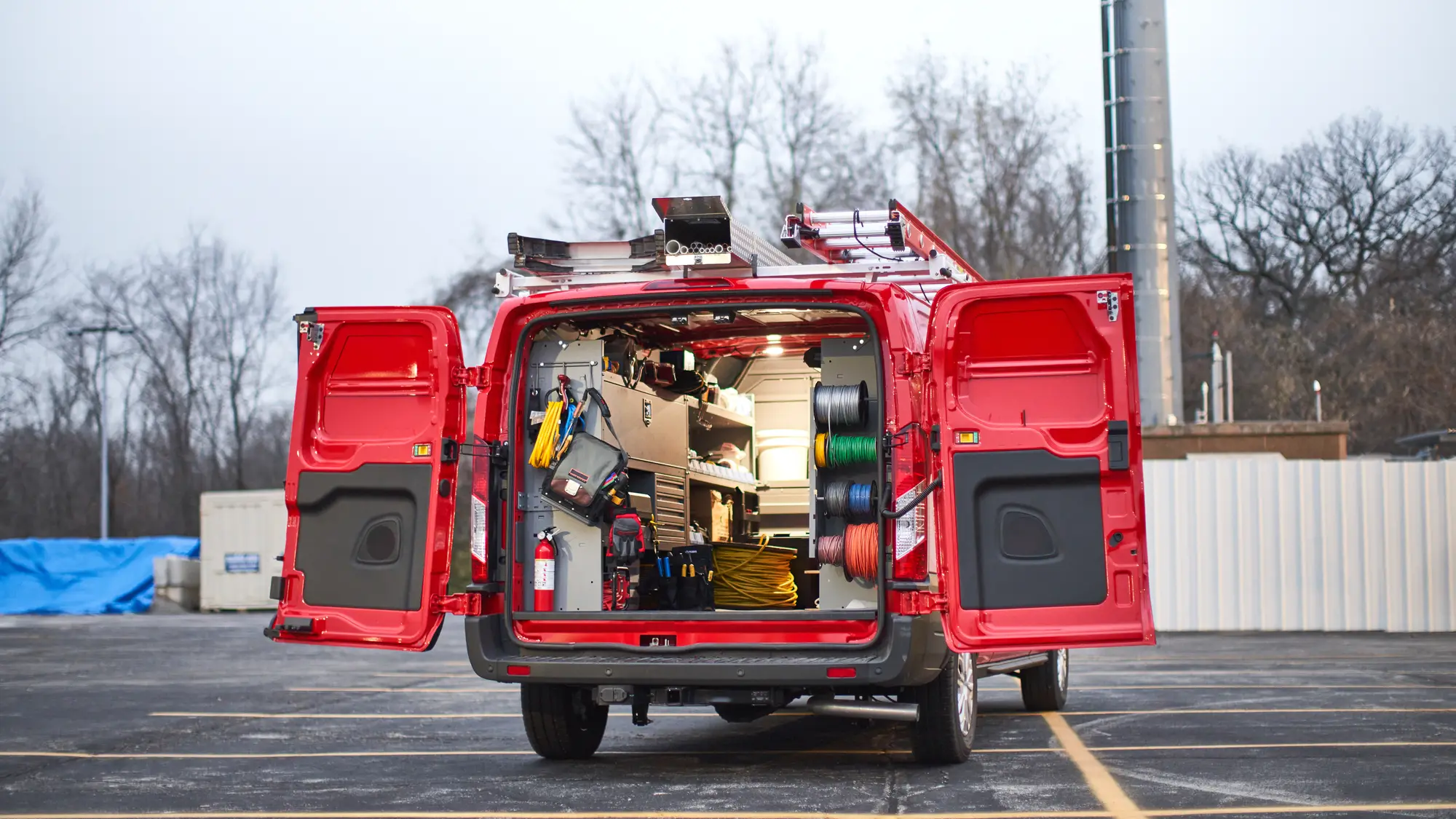 Red telecom work van with rear doors open, showing a complete trade upfit with shelving, reels, and a roof ladder rack