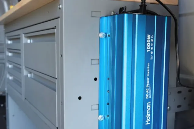 Close-up of a 1000-watt Holman power inverter mounted to the side of a van drawer cabinet
