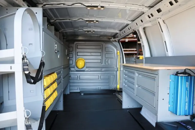 Van cargo area with a Holman drawer cabinet, workbench, and a blue power inverter mounted to its side