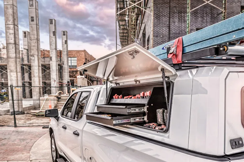 SmartCap side door open on a work pickup, with a slide-out drawer of tools and a ladder on the roof rack