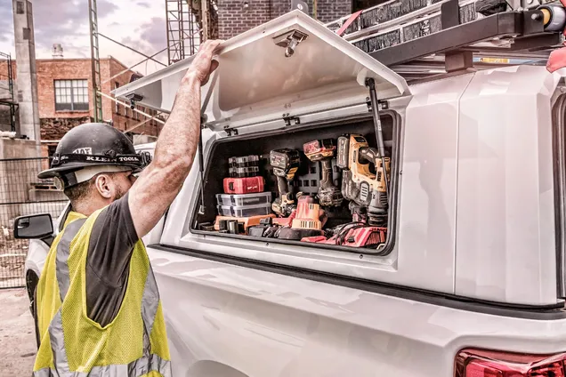 Worker in a safety vest lifting the gullwing side door of a SmartCap to reach power tools stored in the bed