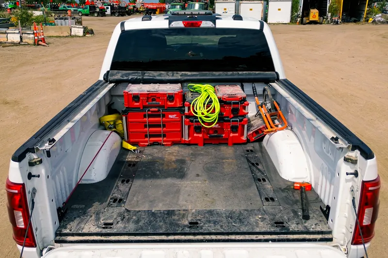 Rear view of a white pickup with the tailgate down, showing Milwaukee Packout cases and gear secured in the bed