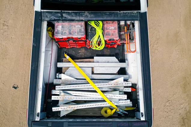 Overhead view of an organized pickup bed with Milwaukee Packout cases, strapped rack parts, and a retractable bed cover