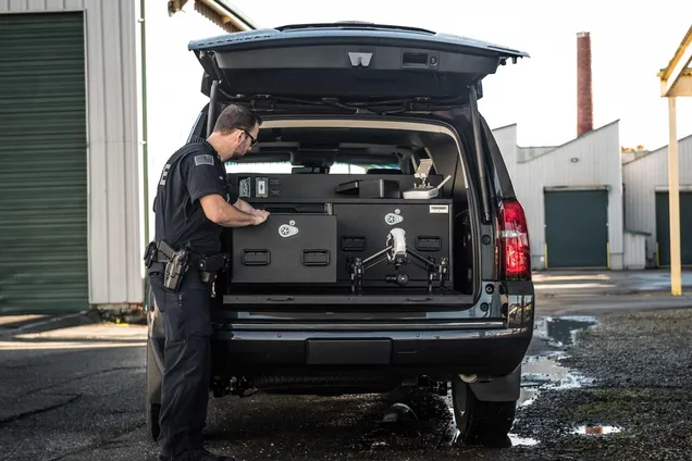 Officer loading equipment into a multi-drawer TruckVault system in the back of a black SUV